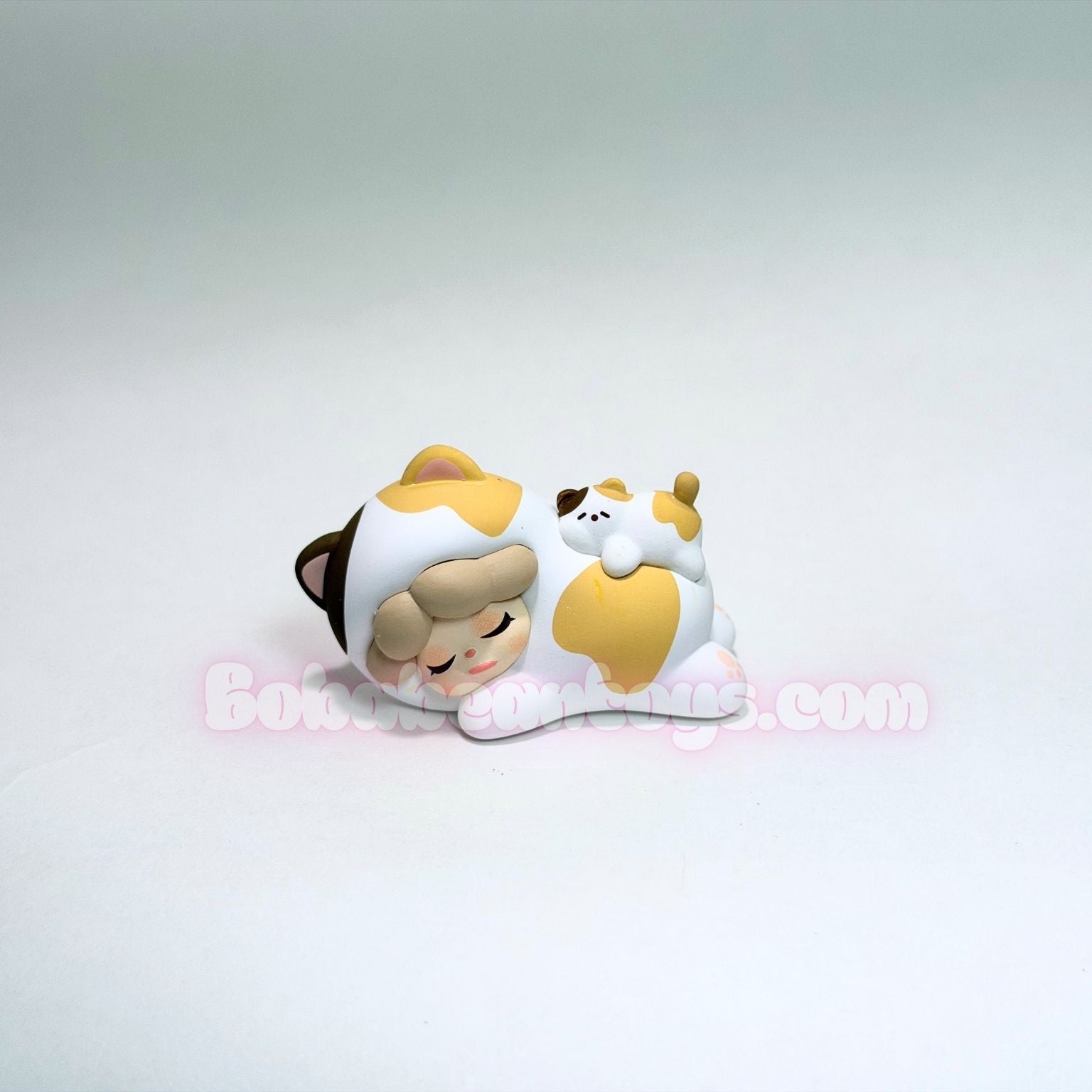 Two small figurines of a cat lying down on a white background