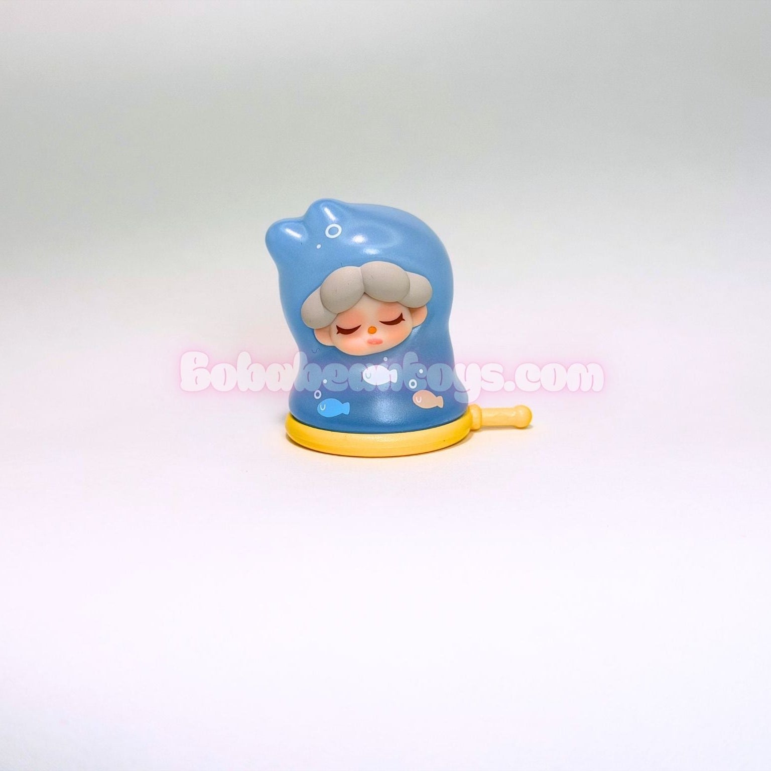 Toy figure of a character with a blue hood and yellow base on a white background