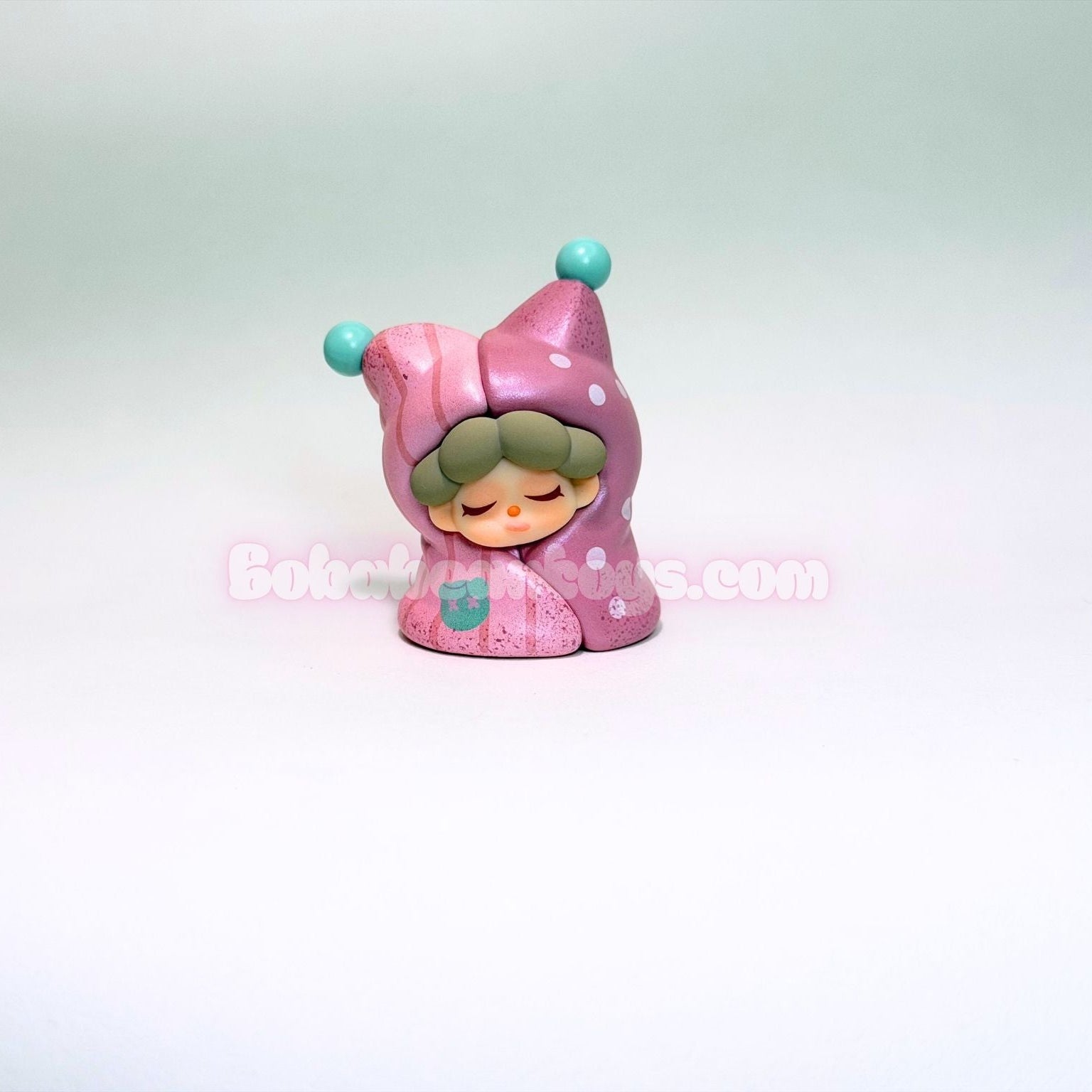 Small figurine of a character in a pink outfit with a blue hat on a light gray background