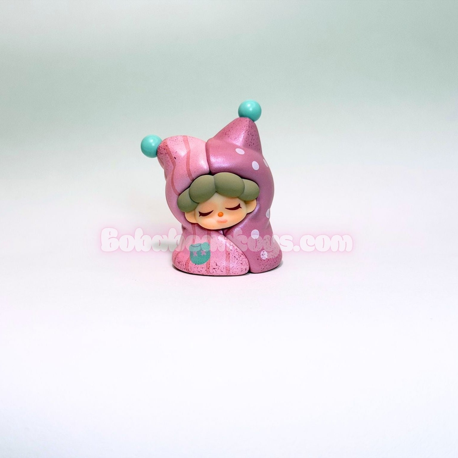 Small figurine of a character in a pink outfit with a blue hat on a light gray background