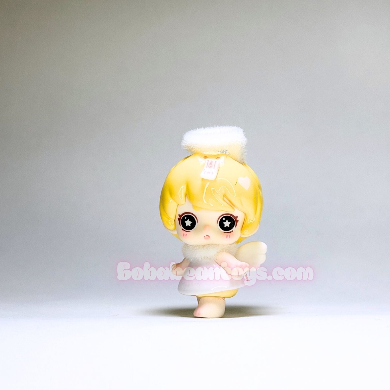 Small figurine with blonde hair and a white outfit on a plain background