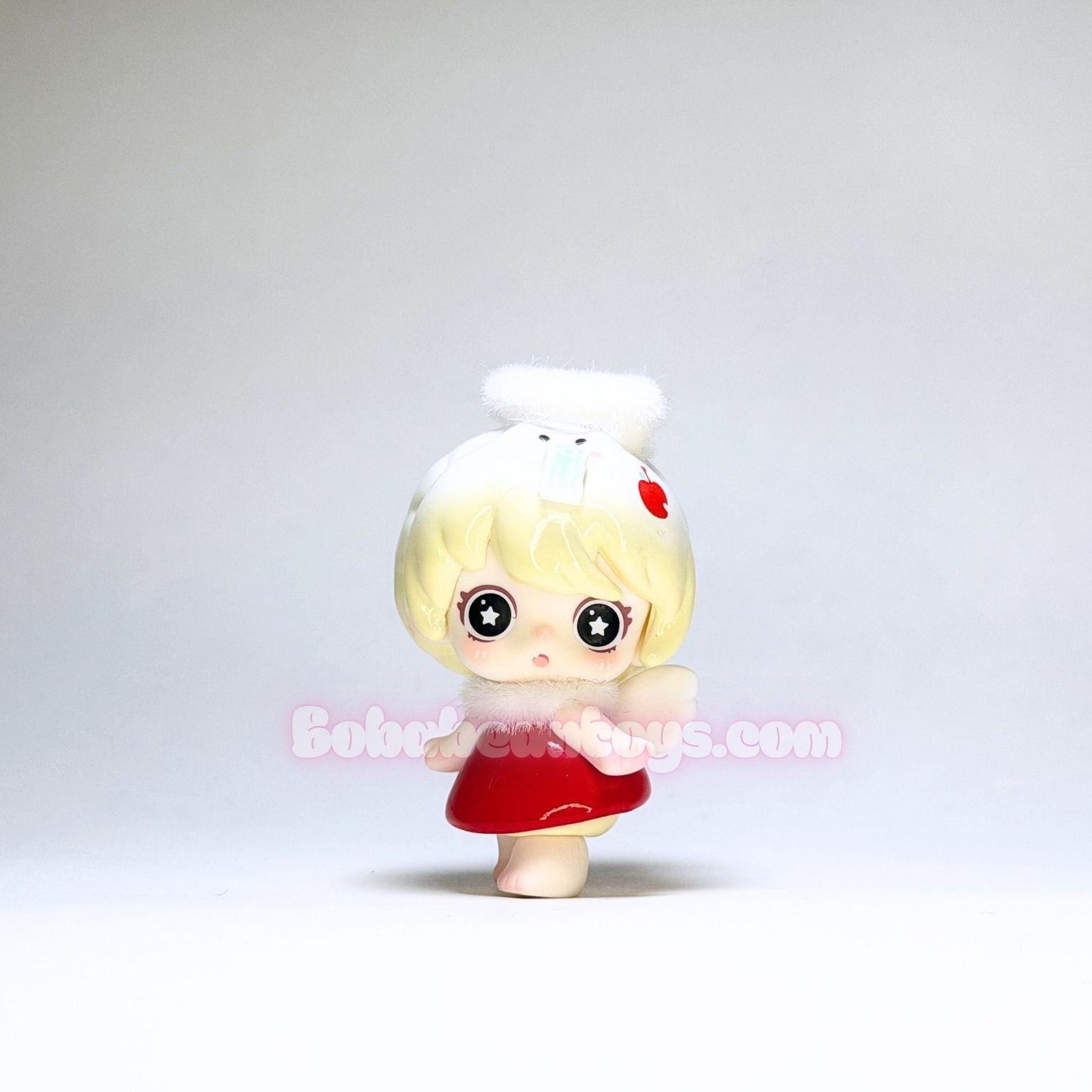 Small figurine with blonde hair and a red dress on a plain background