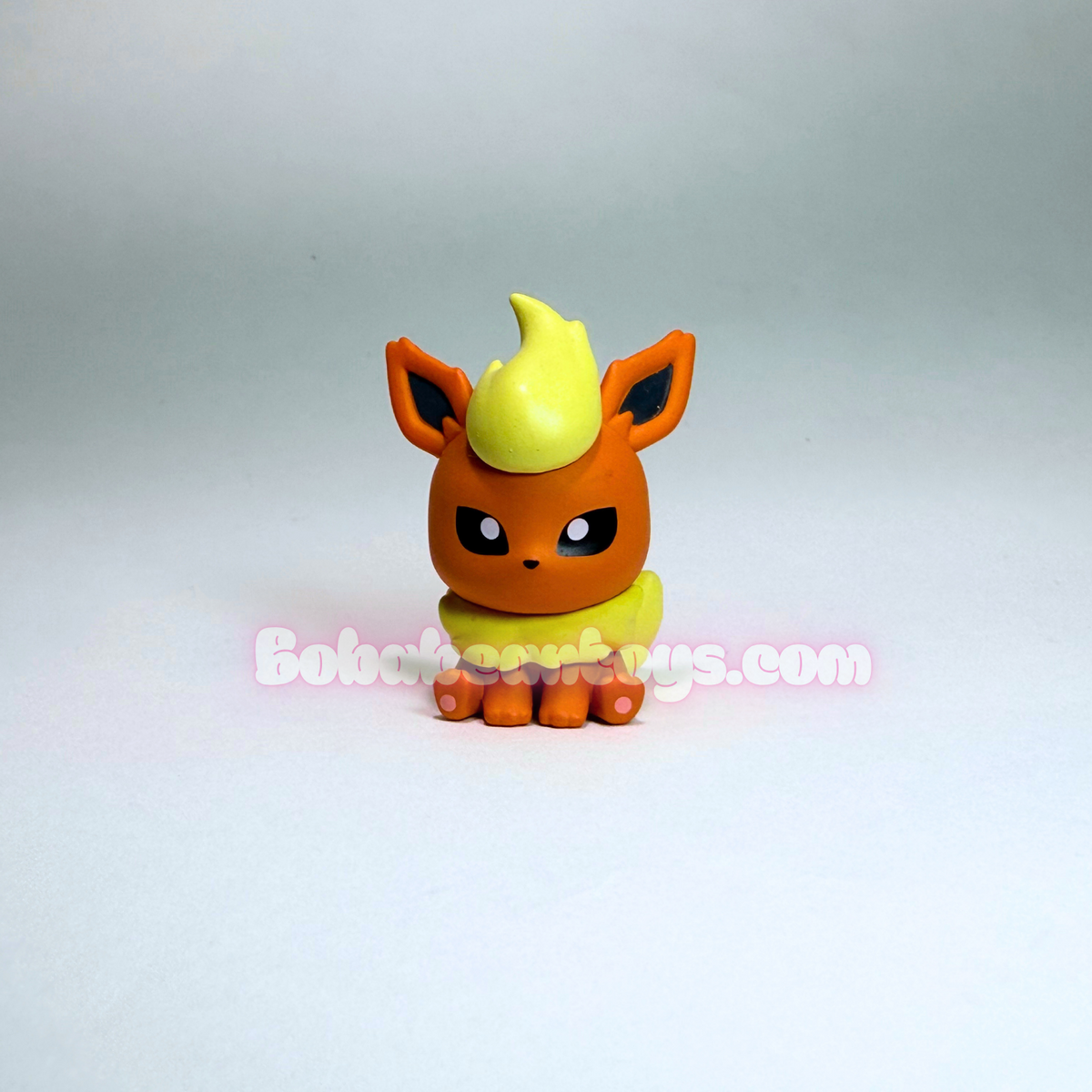 A small orange and yellow Eevee toy figurine standing against a plain light gray background, with a visible 'BokokeToys.com' watermark across the center.