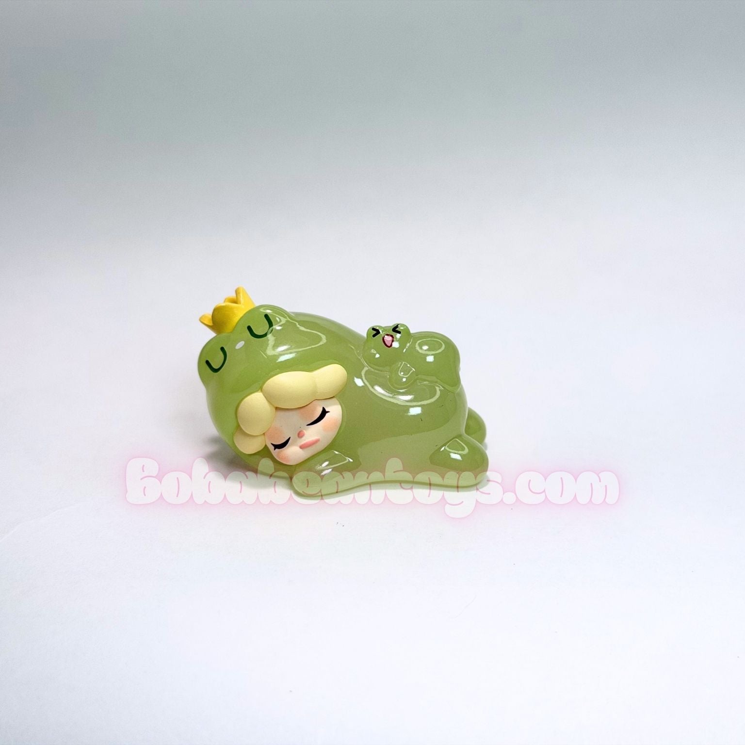 Small green frog figurine with a yellow crown on a white background
