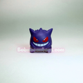 A small purple Gengar toy figure with red eyes and a wide grin, photographed against a plain light gray studio background. A semi-transparent 'BobbeanToys.