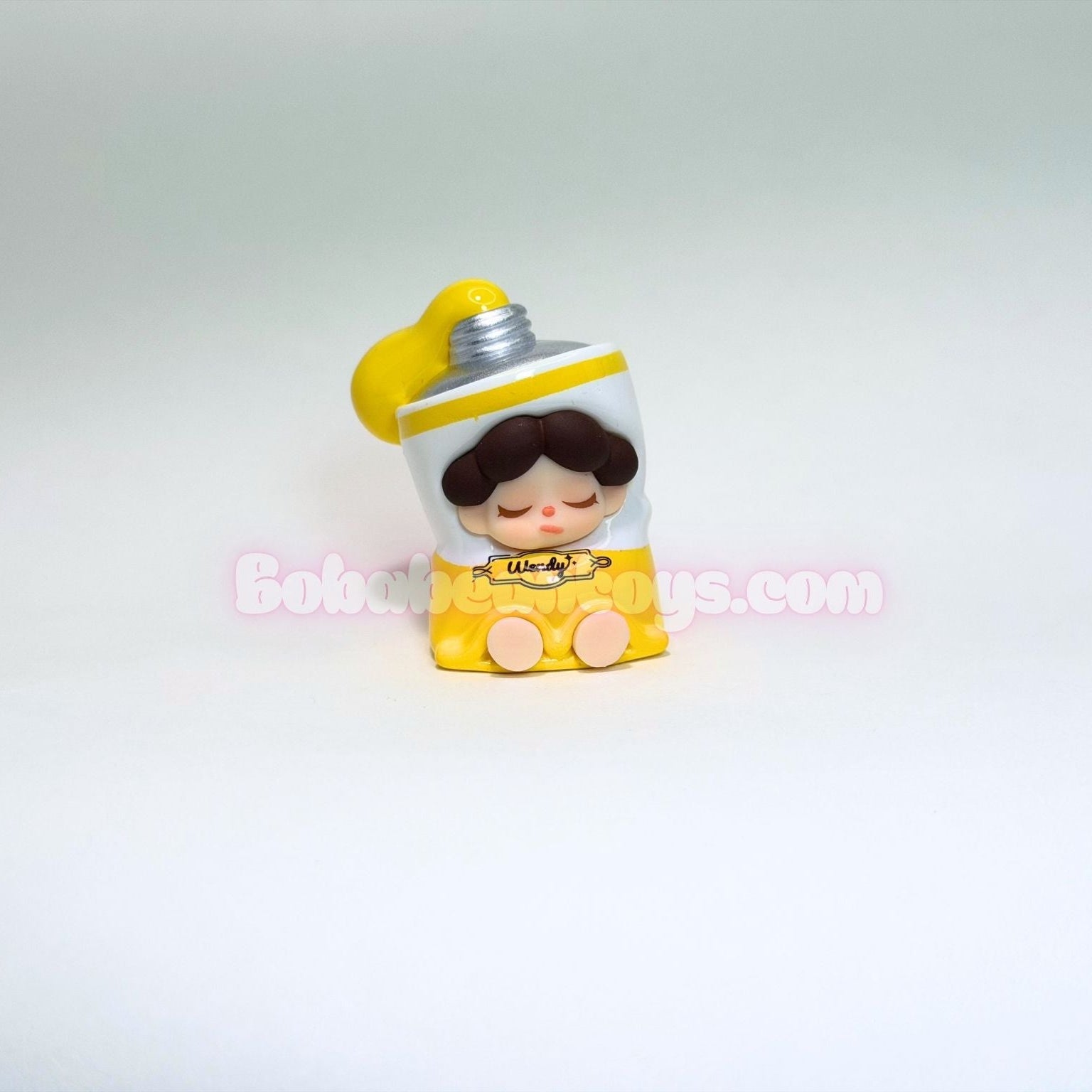 Small figurine of a tube of yellow paint and white outfit on a light gray background
