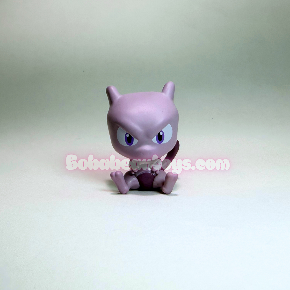 A small purple Mew figurine with blue eyes, sitting on a plain light gray background. A semi-transparent watermark reading 'Bobobo Toys.