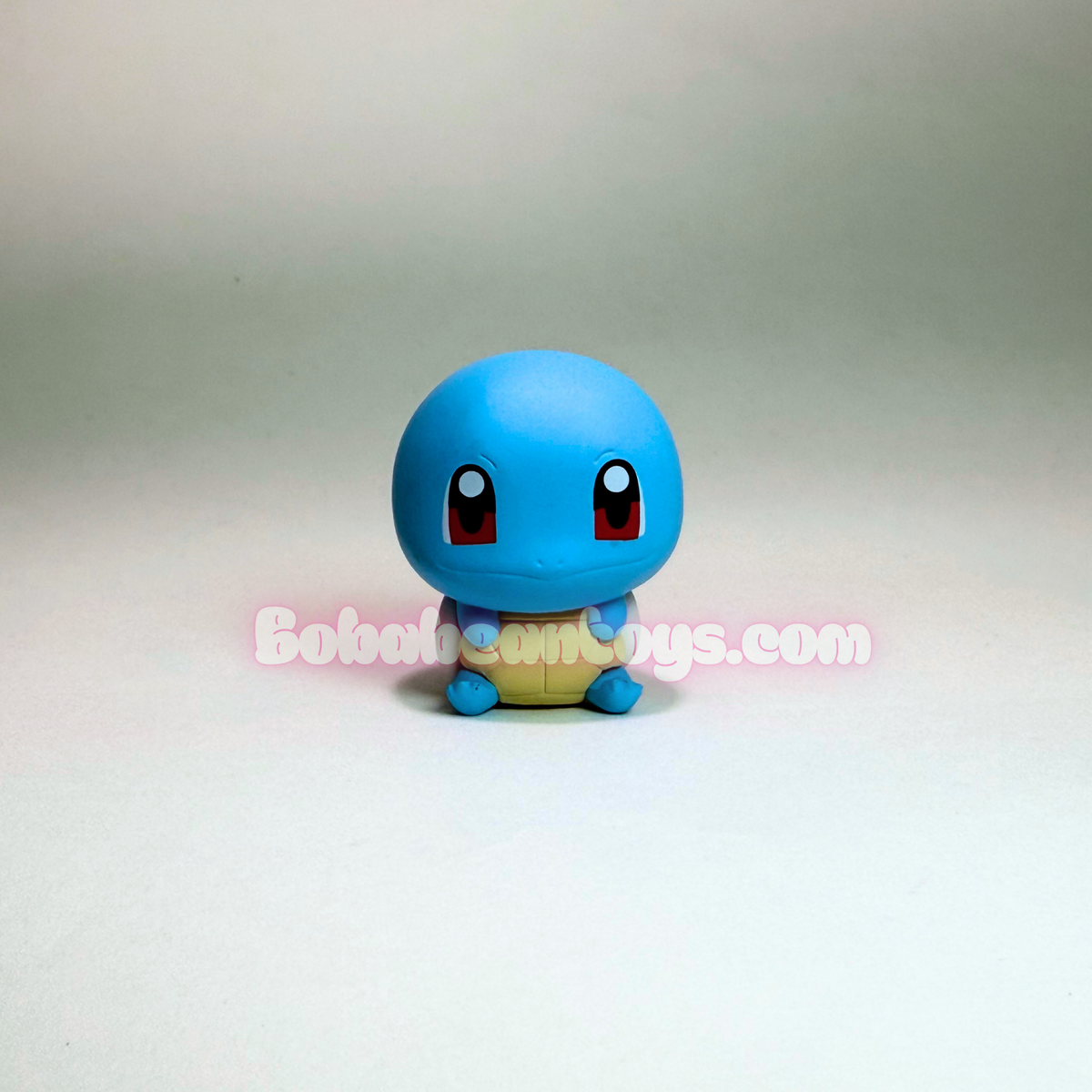 A small blue Squirtle toy figure with a yellow shell and red eyes, photographed against a plain light gray studio background. A pink watermark reading BoboTosToys.