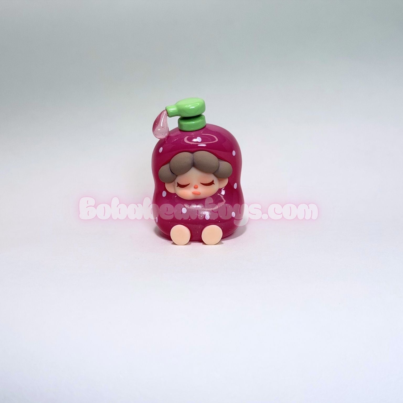 Small figurine of a pink soap bottom and green hat on a white background