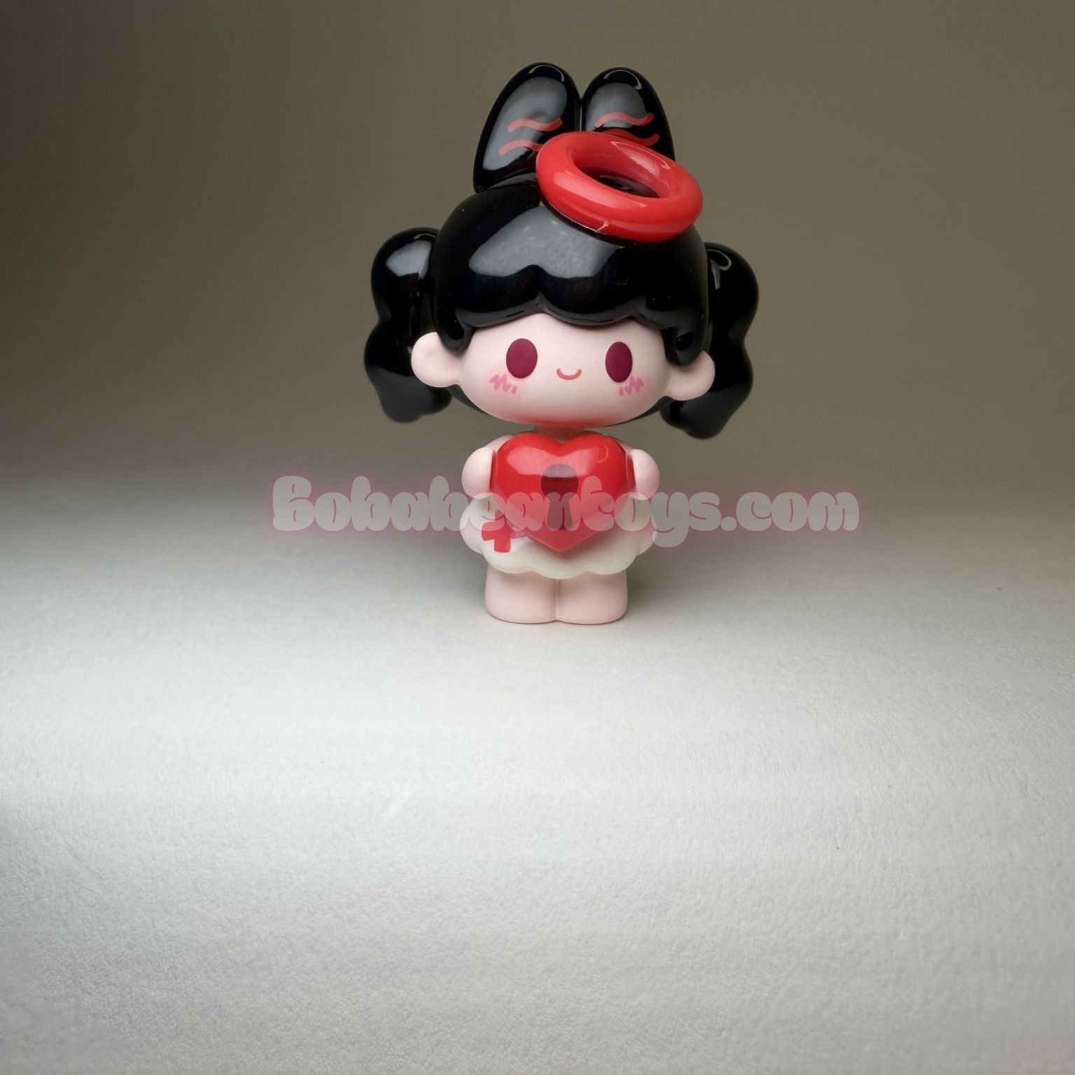 Small figurine with black hair, red heart,  on a gray background