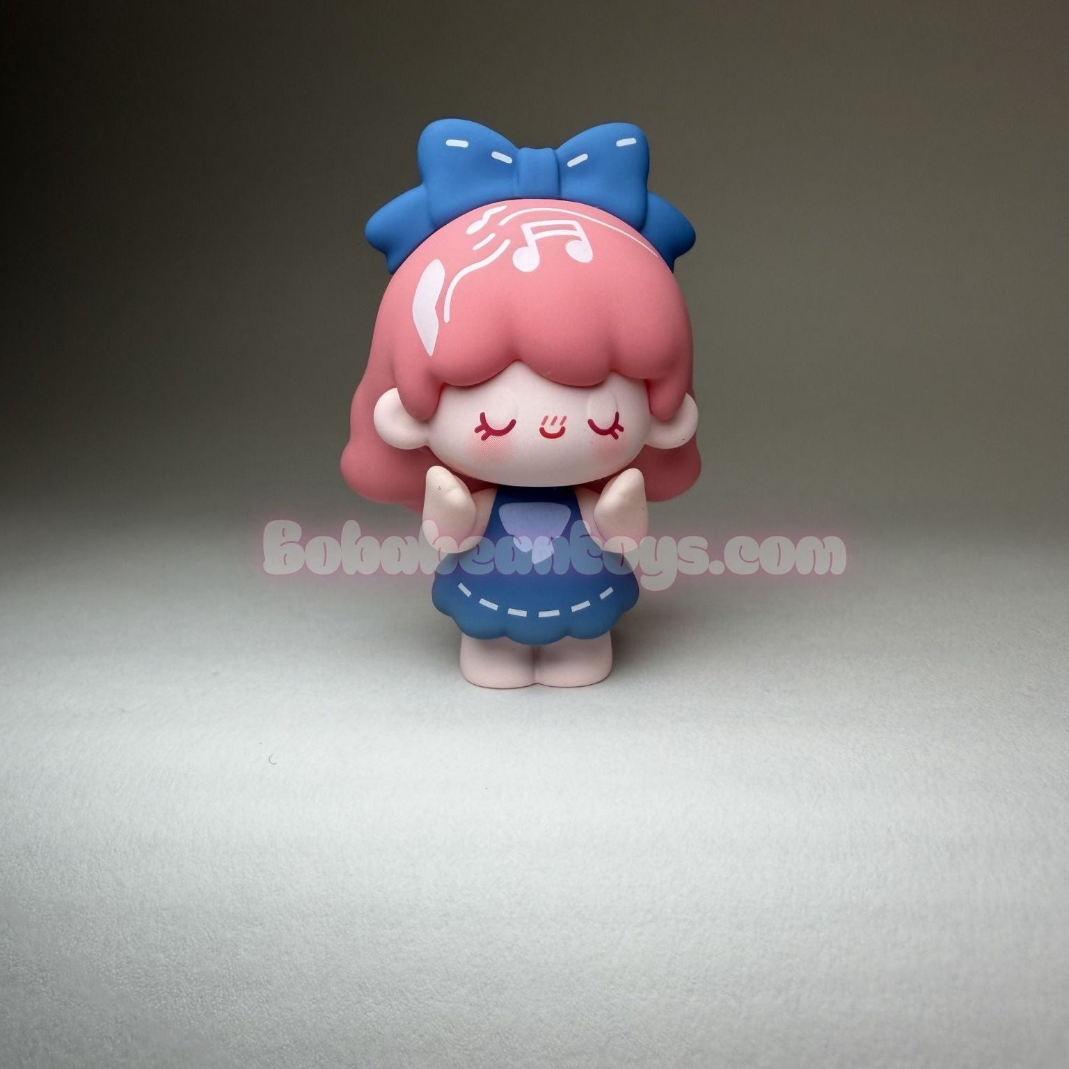 Small figurine with red hair and a blue bow on a gray background